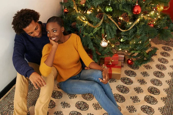 Navidad con la persona que ama. Foto de una pareja joven y cariñosa sentada junto a un árbol de Navidad. —  Fotos de Stock