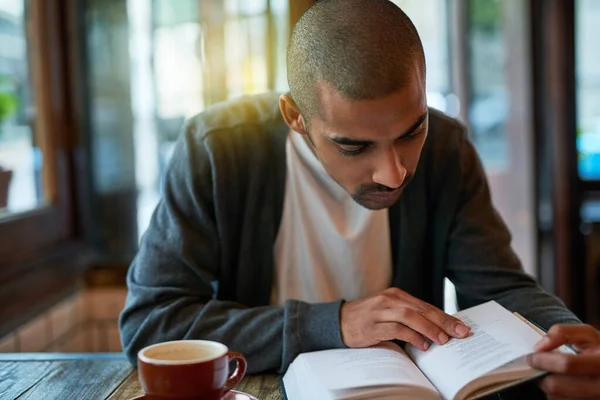 Ez az ő csendes helye távol a világtól. Vágott kép egy fiatalemberről, aki könyvet olvas egy kávézóban.. — Stock Fotó