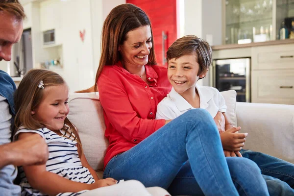 Bonos familiares. Foto de padres sonrientes sentados con su hijo pequeño y su hija en su sofá de la sala de estar en casa. — Foto de Stock