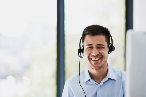 Criando uma experiência de atendimento ao cliente sem esforço. Retrato de um jovem feliz usando um fone de ouvido e usando um computador no trabalho. — Fotografia de Stock