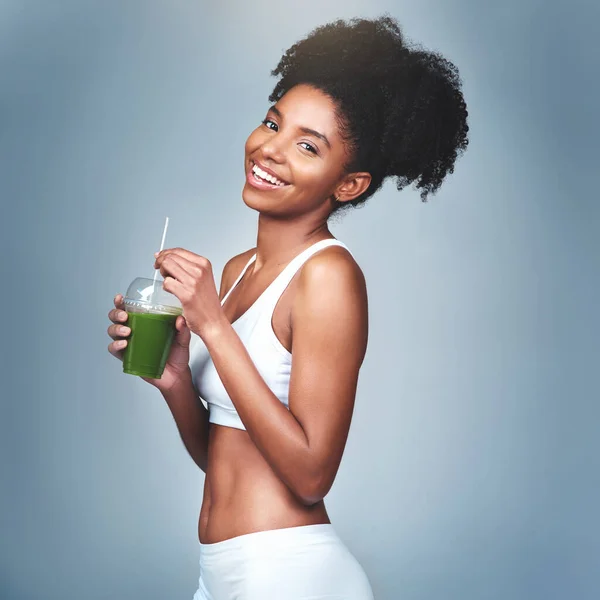 I cant go a day without my green juice. Studio shot of an attractive young woman drinking green juice against a grey background. — Stock Photo, Image