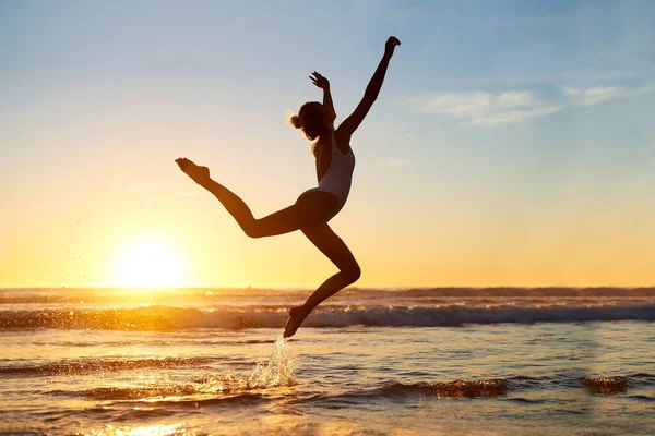 Kau bebas menjadi siapapun. Ditembak seorang wanita muda melompat ke udara terhadap matahari terbenam yang indah di pantai. — Stok Foto