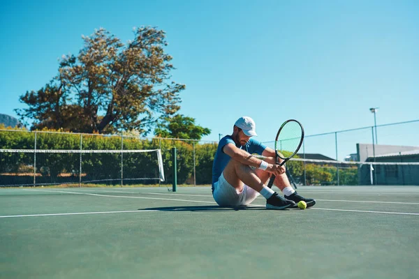 Никто не проиграет, пока не перестанет пытаться. Полнометражный снимок молодого теннисиста, усталого и сидящего на теннисном корте на открытом воздухе. — стоковое фото