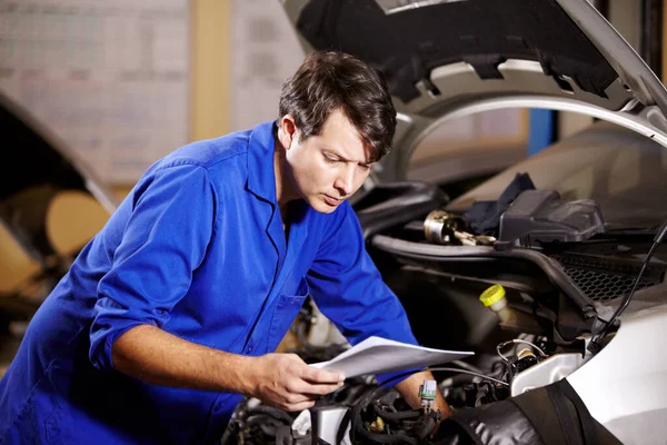 Ik kan beter de bedrading controleren. Een mannelijke monteur leest wat papieren terwijl hij aan de motor van een auto werkt. — Stockfoto