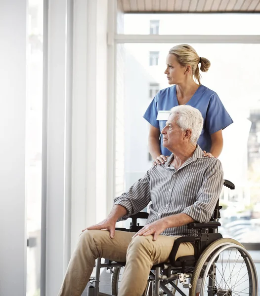 Σιγουρεύομαι ότι δεν είναι κλεισμένος στο δωμάτιο ανάρρωσης. Τραβηγμένο πλάνο μιας ώριμης νοσοκόμας και του ανώτερου ανδρικού ασθενούς με αναπηρική καρέκλα στο νοσοκομείο. — Φωτογραφία Αρχείου