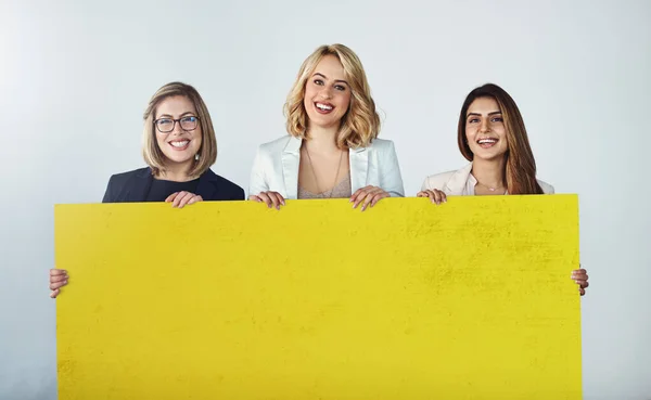 Sostenuta dai professionisti del settore. Studio foto di un gruppo di donne d'affari che reggono un cartello giallo vuoto. — Foto Stock