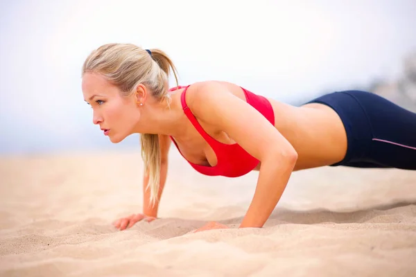 Salud del cuerpo entero. Fotografía de una joven en ropa deportiva haciendo flexiones en la playa. — Foto de Stock