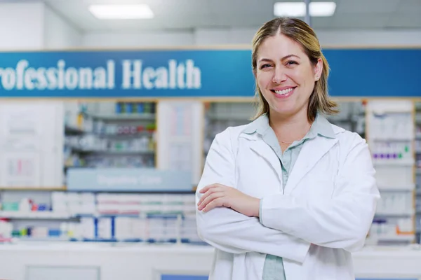 Vždy si vybírejte lidi, kteří upřednostňují vaše blaho. Portrét mladé lékárnice, usmívající se a pózující se založenýma rukama v lékárně. — Stock fotografie