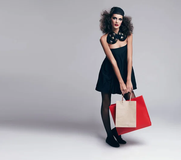 Haute Couture ist ihr Stil. Studioporträt eines schönen jungen Models, das Einkaufstüten vor grauem Hintergrund trägt. — Stockfoto