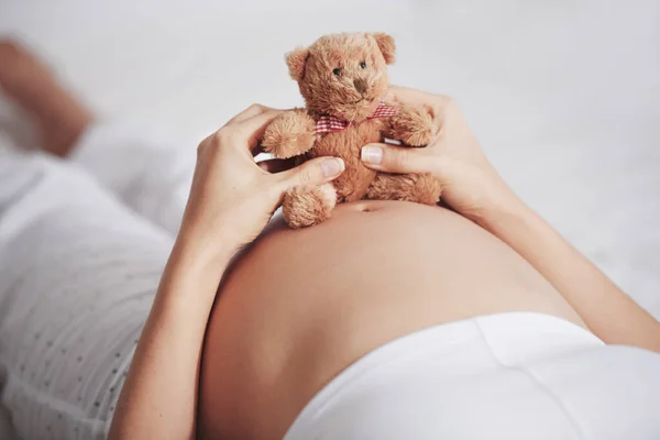 Vinculación de bulto de bebé. Un disparo de una mujer embarazada sosteniendo un osito de peluche encima de su vientre. — Foto de Stock
