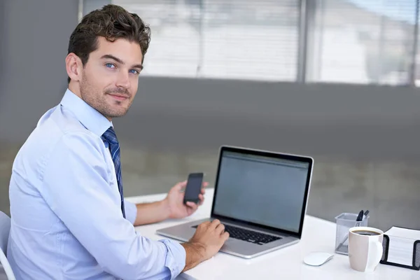 Una buena comunicación con el cliente es su prioridad. Retrato de un joven empresario sentado en su escritorio con un teléfono móvil en la mano. — Foto de Stock