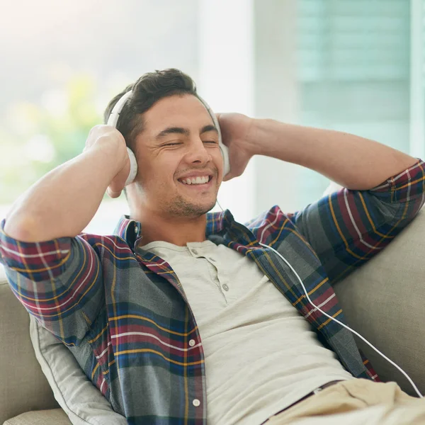 Desliga a semana, aumenta a música. Tiro de um jovem relaxando no sofá e ouvindo música com fones de ouvido em casa. — Fotografia de Stock