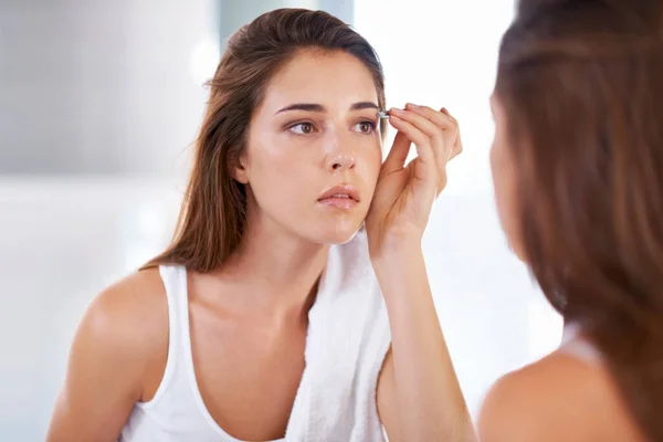 Dándoles forma a la perfección. Una joven pinza sus cejas frente a un espejo. — Foto de Stock