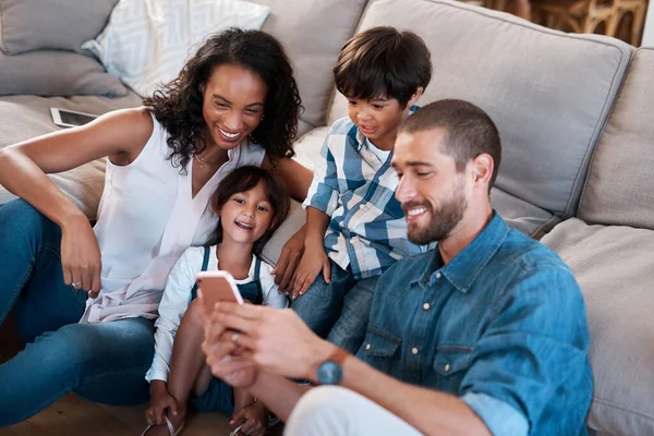 Kijk hier eens naar. Een foto van een gezin van vier kijkend naar iets op een mobiele telefoon.. — Stockfoto