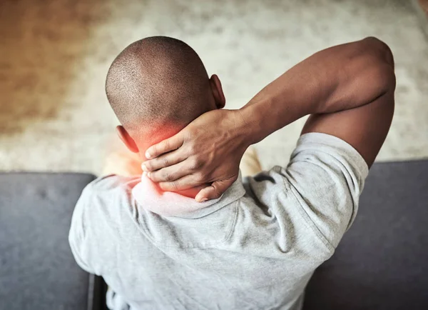 Ik moet vannacht verkeerd geslapen hebben. Achteraanzicht van een onherkenbare man die zijn nek ongemakkelijk vasthoudt terwijl hij thuis op een bank zit. — Stockfoto