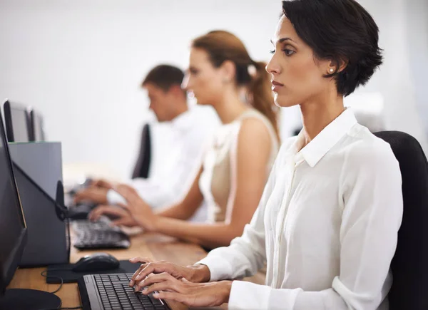 Geballte Belegschaft. Aufnahme einer attraktiven jungen Büroangestellten am Computer mit ihren Kollegen im Hintergrund. — Stockfoto