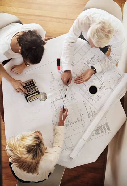 Plannen van hun volgende stap. Hoge hoek opname van een groep architecten die samenwerken op blauwdrukken van een huis rond een tafel in een gebouw. — Stockfoto