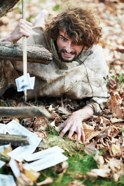 Ces feuilles n'ont rien à faire ici. Un homme des cavernes à l'air fou rampant sur le sol et perçant de l'argent avec sa lance. — Photo