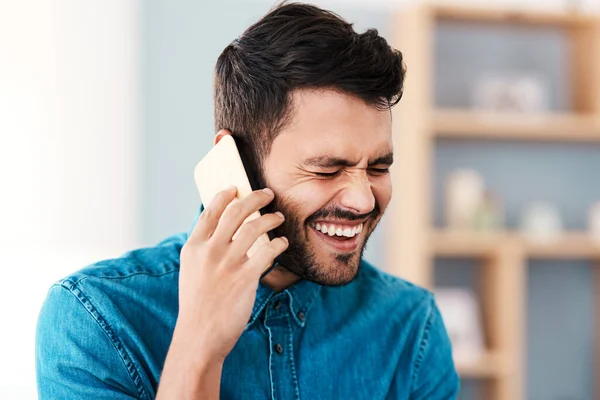 Thats incredibly hilarious. Cropped shot of a handsome young man laughing while taking a phonecall in his living room at home. — Stock Photo, Image