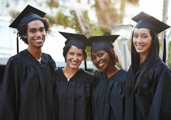 Tienen un futuro brillante por delante. Un grupo de graduados de la universidad sonrientes de pie juntos en la tapa y el vestido. — Foto de Stock