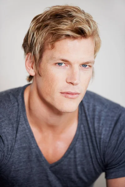 Eyes like a hawk. Portrait of a handsome young man sitting against a grey background. Stock Image