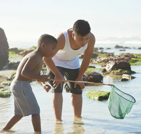 自分の夕食をキャッチします。父親と彼の息子の網で釣りのショットは、ビーチで. — ストック写真