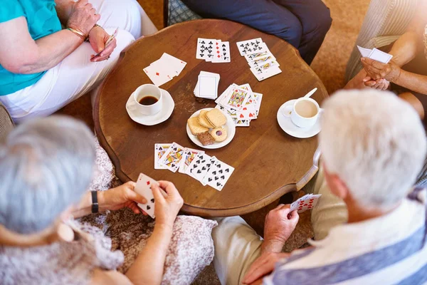 Ganhar através de uma combinação de sorte e habilidade. Tiro de ângulo alto de um grupo de idosos jogando cartas em torno de uma mesa em sua casa de repouso. — Fotografia de Stock