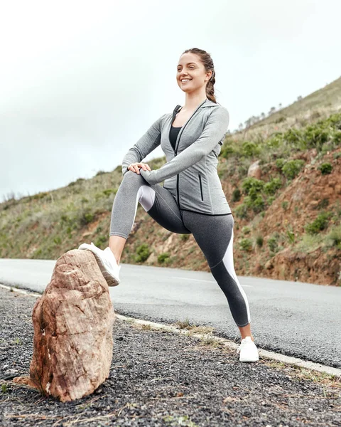 Att springa med muskler som inte är ordentligt förberedda kan leda till påfrestningar. Skjuten av en sportig ung kvinna som sträcker på benen när hon tränar utomhus. — Stockfoto