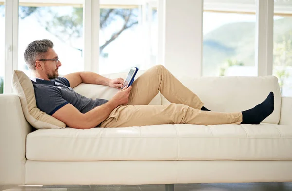 Sofa surfing.... Shot of a man using his tablet while relaxing on the sofa at home. — Stock Photo, Image