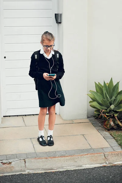 Aspetto pazientemente che arrivi il mio passaggio a scuola. Scatto completo di una giovane studentessa che ascolta musica e usa il cellulare mentre si trova fuori casa. — Foto Stock