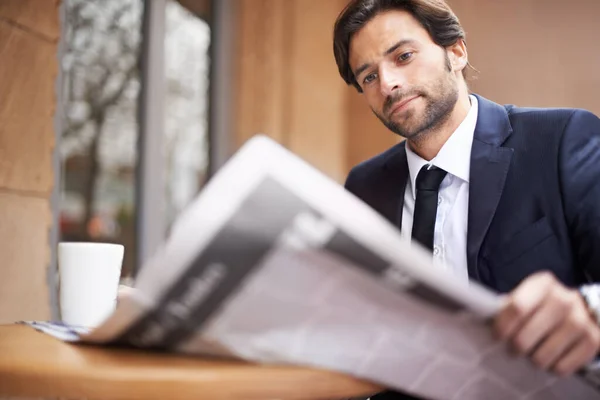 Lo que está pasando en el mundo de los negocios hoy. Un joven empresario leyendo un periódico al aire libre en una cafetería. —  Fotos de Stock