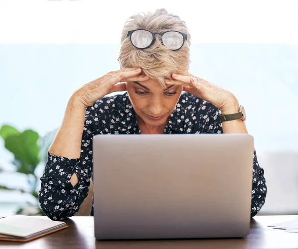 Cela ne peut pas arriver en ce moment. Prise de vue d'une femme mature assise seule et stressée alors qu'elle utilisait son ordinateur portable pour travailler à la maison. — Photo