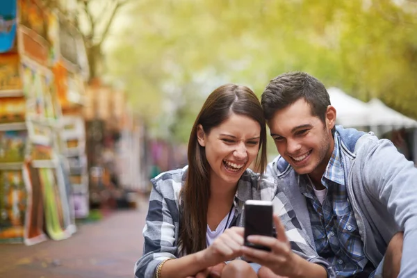 让我们抓住这一刻。一对快乐的年轻夫妇坐在外面看手机上的照片. — 图库照片
