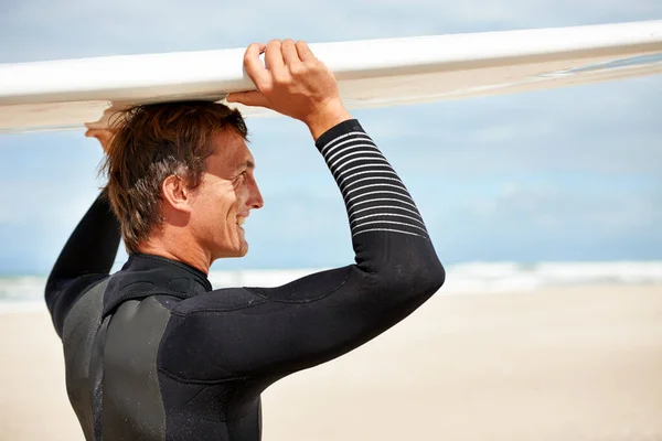 Es sind nur ich und mein Surfbrett. Aufnahme eines lächelnden jungen Surfers am Strand, der sein Brett auf dem Kopf trägt. — Stockfoto
