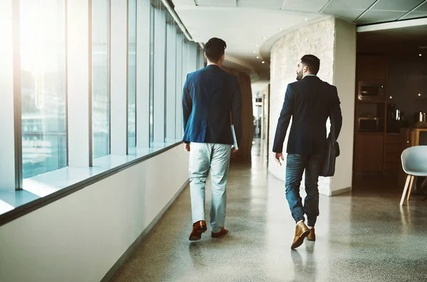 O sucesso não acontece até que as pessoas se movam. Foto retrovisada de dois jovens empresários caminhando por um corredor de um escritório moderno. — Fotografia de Stock