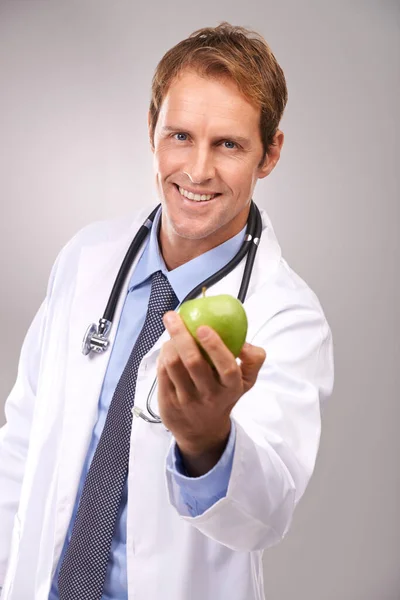 Um por dia vai manter-me afastado. Retrato de estúdio de um belo jovem médico segurando uma maçã verde. — Fotografia de Stock