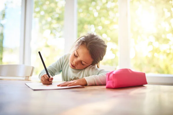 Haar creativiteit aanwakkeren. Opname van een gefocust klein meisje dat tekeningen maakt in een boek terwijl ze thuis aan een tafel zit. — Stockfoto