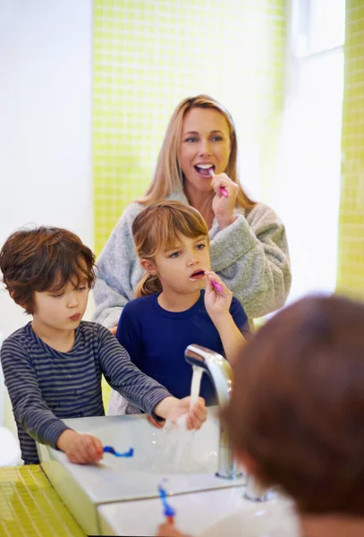 Teaching them the importance of oral hygiene. Shot of a young family brushing their teeth in the bathroom. — Stock Photo, Image