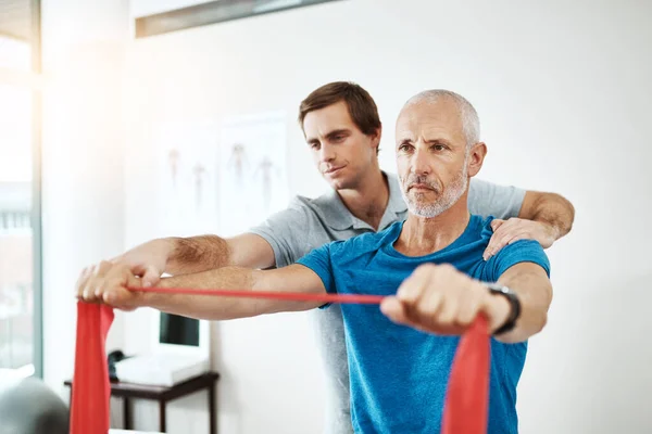 Halten Sie den Rücken gerade. Aufnahme eines jungen männlichen Physiotherapeuten, der einem Klienten tagsüber bei Dehnübungen in seinem Büro hilft. — Stockfoto