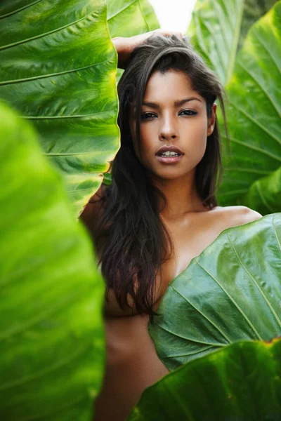 Tropiklerde üstsüz. Üstsüz vücudunu yeşil bir yaprağın arkasına saklayan genç ve güzel bir etnik kadın.. — Stok fotoğraf
