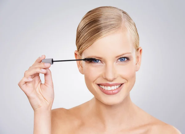 Adding mascara to her eyelashes. A beautiful young woman in the studio. — Stock Photo, Image