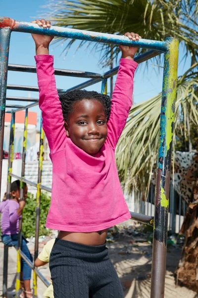 Holding on tight to carefree days of youth. Portrait of a happy little girl hanging on a jungle gym. — Stock Photo, Image