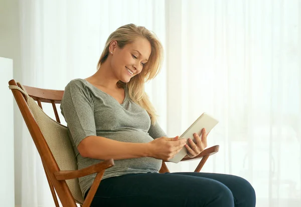 Nechte technologii, ať vás provede celým procesem. Snímek těhotné ženy pomocí svého digitálního tabletu, zatímco sedí na houpacím křesle. — Stock fotografie