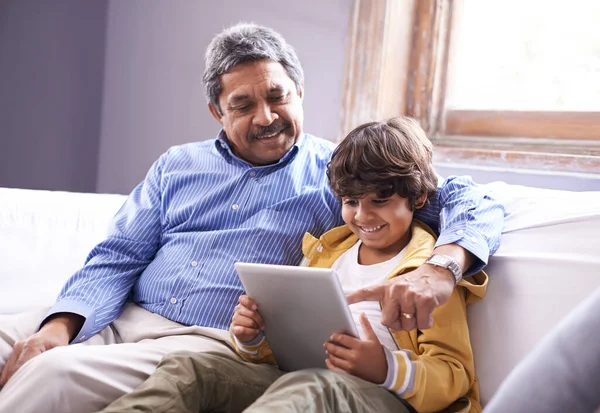 Megmutatni nagyapának, hogy minden poklot be kell kapcsolni. Fényképezte nagyapa és unokája ül a kanapén egy digitális tabletta. — Stock Fotó