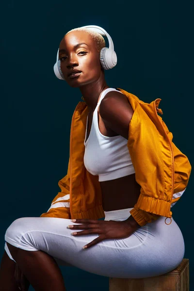 Shes geben dem Vertrauen eine neue Bedeutung. Ausgeschnittenes Porträt einer attraktiven jungen Sportlerin, die allein sitzt und mit Kopfhörern vor dunklem Studiohintergrund posiert. — Stockfoto