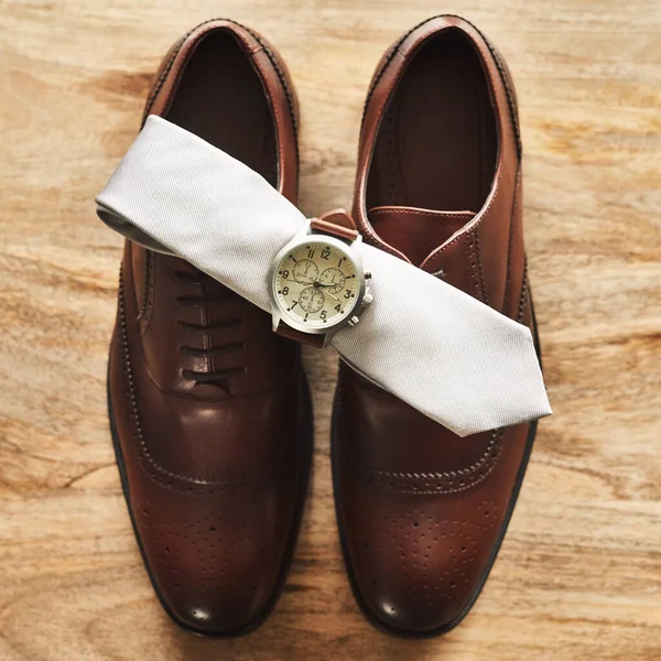 Clássico nunca sai de moda. Tiro de natureza morta de um relógio de pulso e laço em cima de sapatos formais em uma superfície de madeira. — Fotografia de Stock