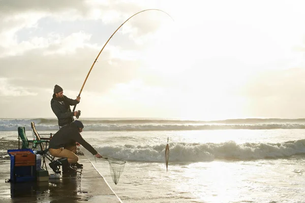 Ive got the big one. Shot of two young men fishing off a pier. — Stock Photo, Image