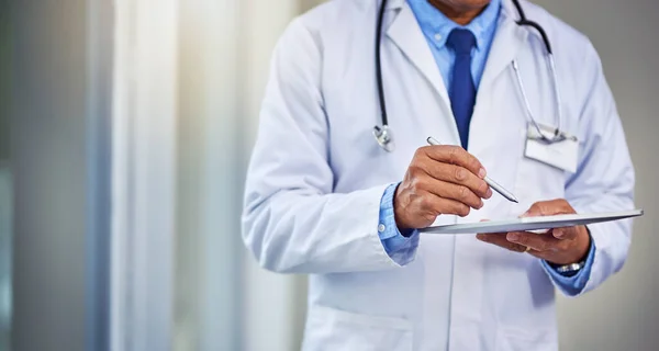 Sus horarios siempre están ocupados. Inyección de un médico masculino irreconocible que escribe en una tableta digital mientras está de pie dentro de un hospital durante el día. — Foto de Stock