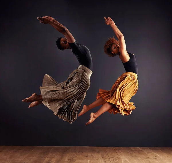 Sincronização. Dois dançarinos contemporâneos realizando um salto sincronizado na frente de um fundo escuro. — Fotografia de Stock