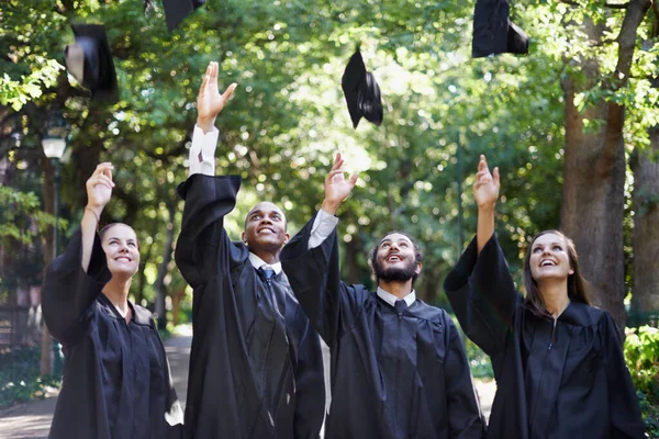 Das Leben beginnt jetzt. Eine Gruppe fröhlicher Universitätsstudenten wirft am Abschlusstag ihre Mützen in die Luft. — Stockfoto